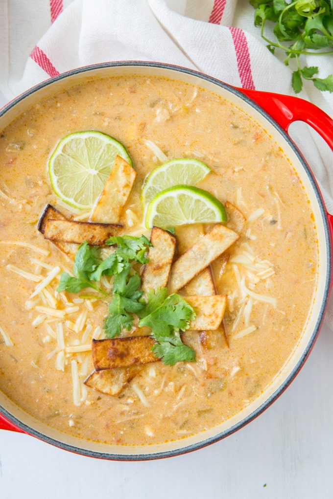 A big pot of chicken enchilada soup topped with limes and tortilla strips