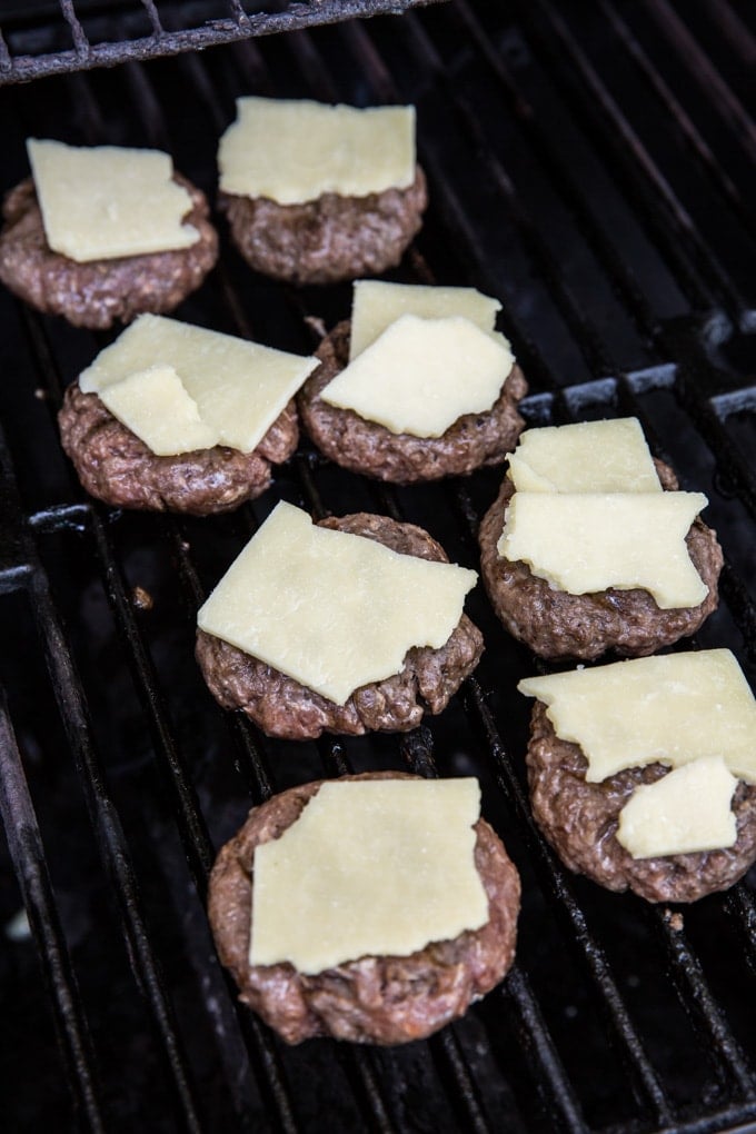 8 hamburger sliders with cheese on a grill.