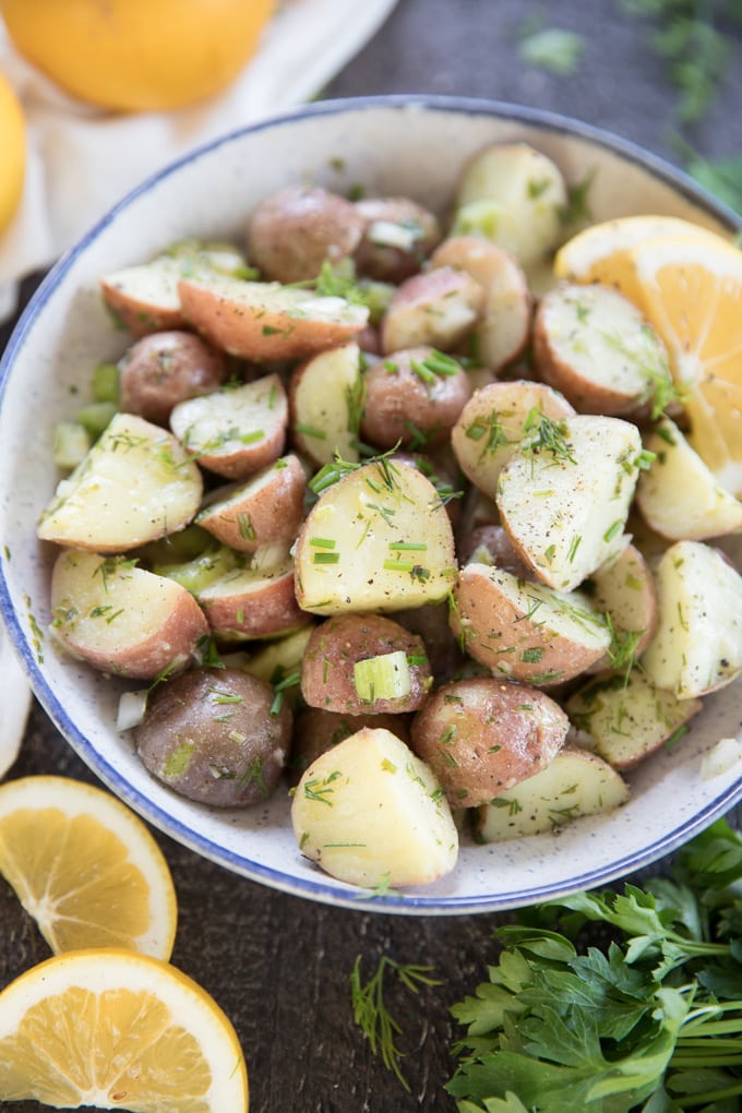 diced red potatoes with dill and green onions, sliced lemons, in a blue and white bowl.