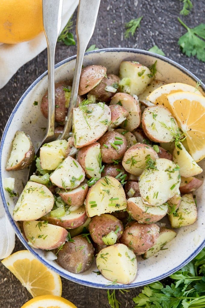 Lemon Herb Red Potato Salad is full of tender potatoes and tons of flavor! Made with an oil based lemon herb dressing and no mayo, it's perfect for summer. Red Potato Salad with lemon and fresh herbs in a blue bowl with silver spoons,