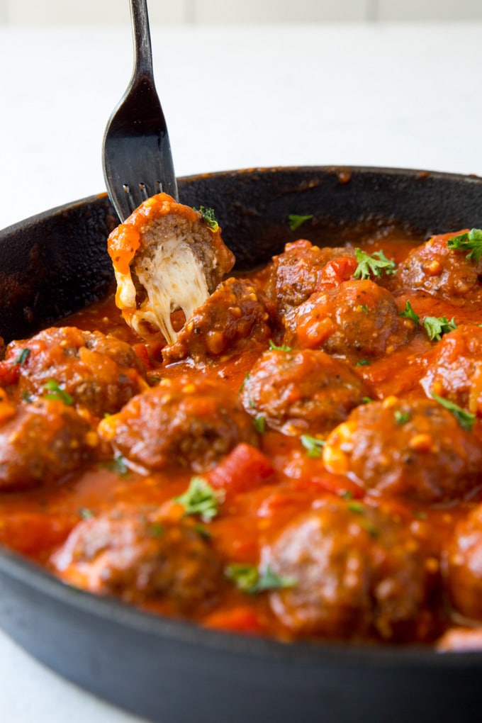 A fork stuck into a cheese stuffed meatball, pulling it out of the pan.