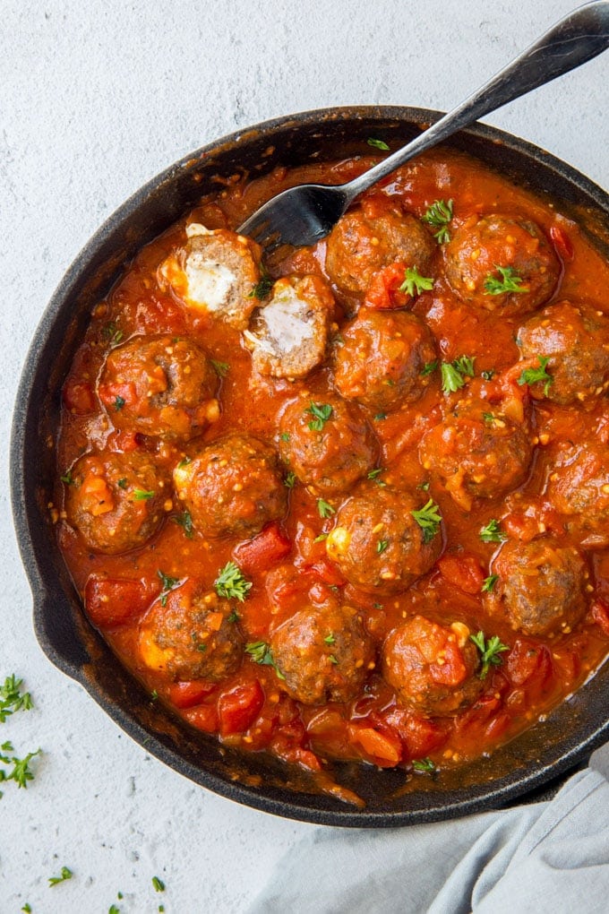 An overhead shot of a skillet with mozzarella stuffed meatballs in marinara sauce. 