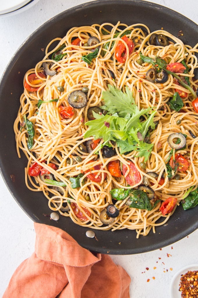 Pasta puttanesca in a skillet topped with fresh arugula