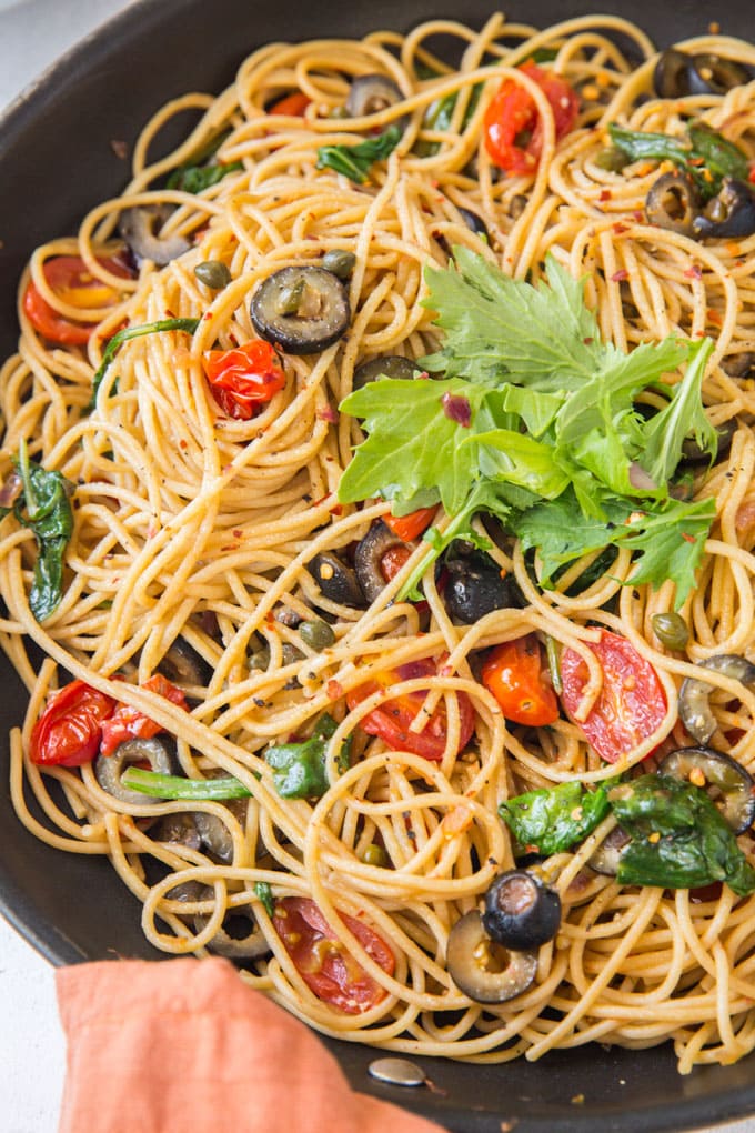 Pasta Puttanesca is a light meal of fresh pasta with lemon juice, tomatoes, spinach and arugula and a robust saltiness from capers and olives. a large skillet filled with fresh pasta puttanesca