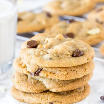 A stack of potato chip cookies with a glass of milk and tray of cookies cooling in the background.