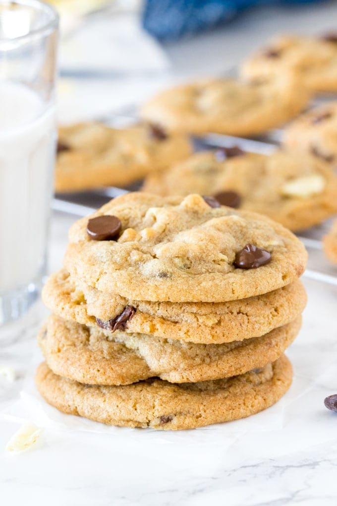A stack of potato chip cookies with a glass of milk and tray of cookies cooling in the background. 