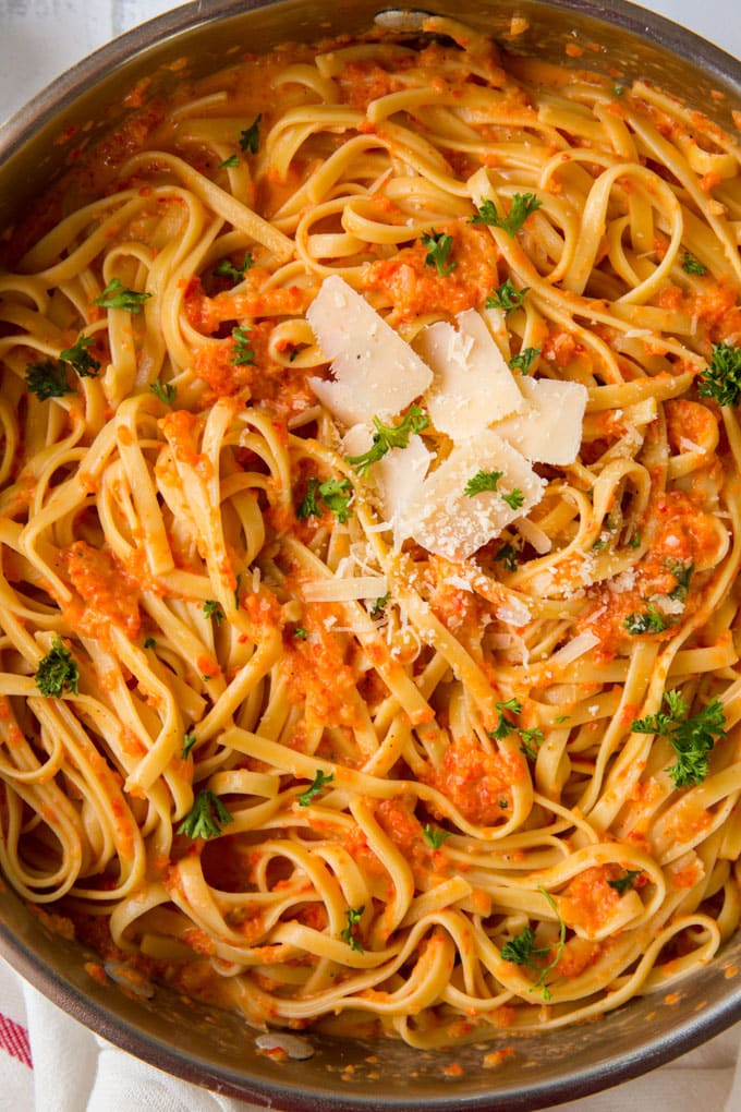 a large saute pan filled with fettuccine pasta with red pepper sauce and parmesan cheese on top.