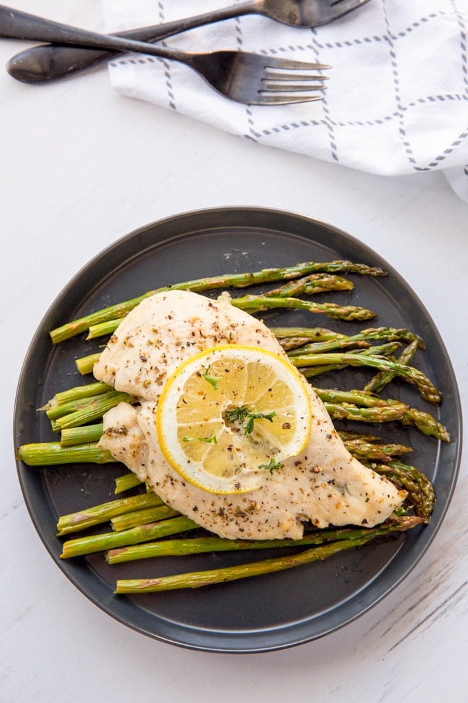 A black plate of food on a table, with Lemon and Chicken and asparagus