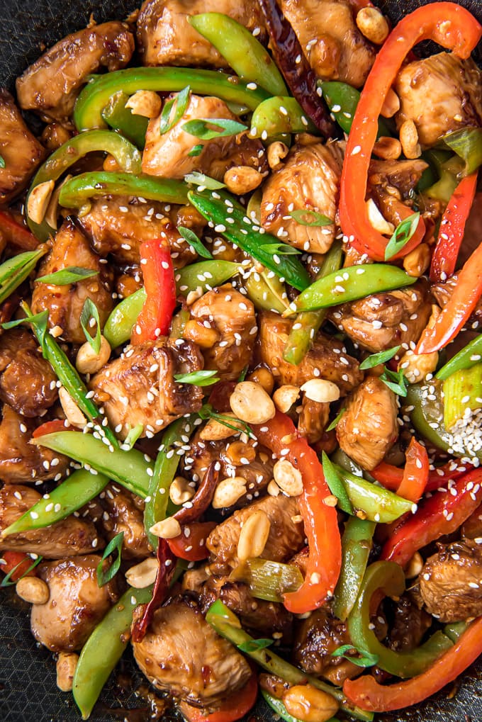 A close up of a wok filled with chicken, vegetables and szechuan sauce.