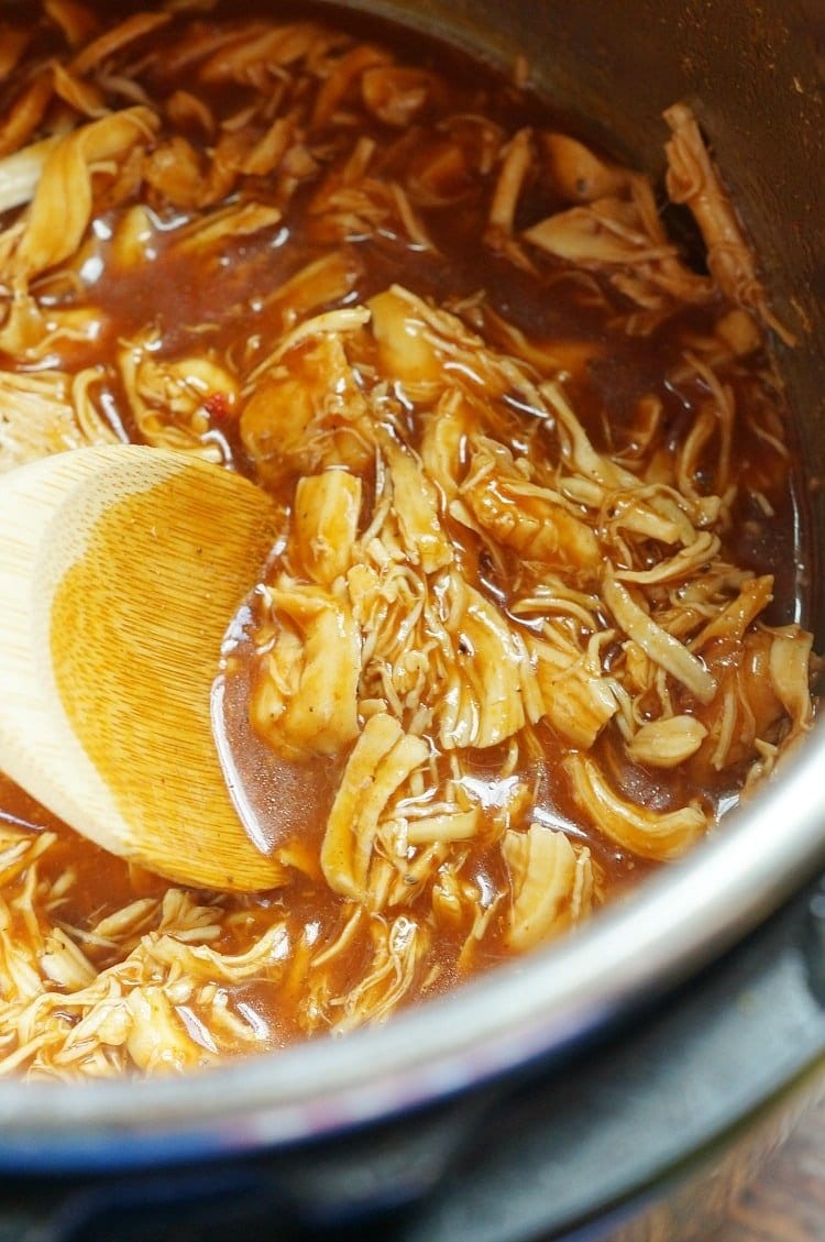 instant pot with shredded chicken, bbq sauce and a wooden spoon