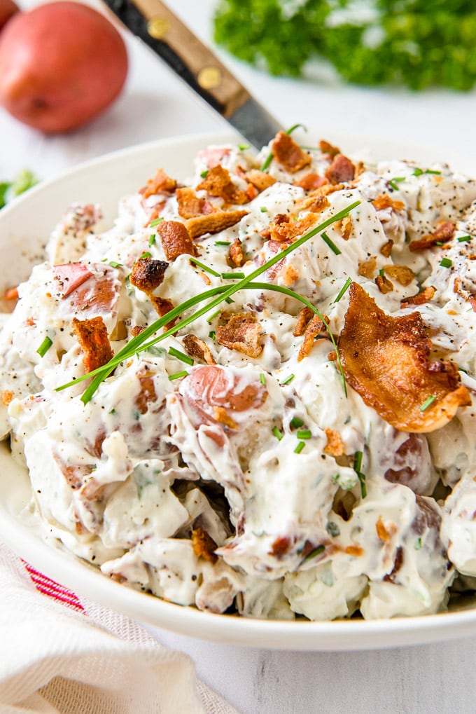 A side view of a bowl of bacon ranch red potato salad with a large spoon.