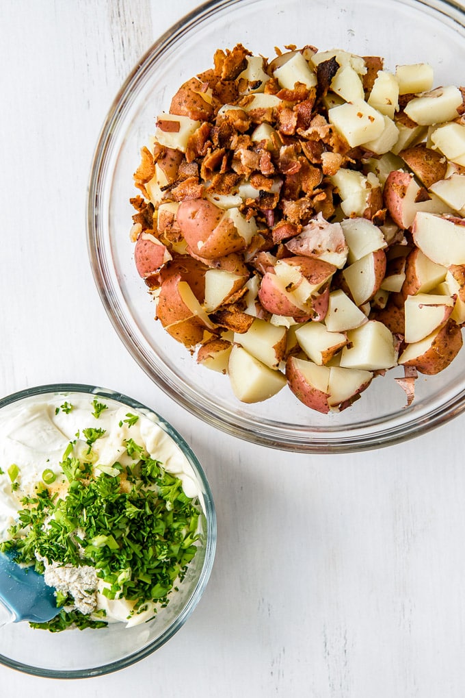 Diced red potatoes with bacon in a bowl, another bowl with sour cream and green onions.