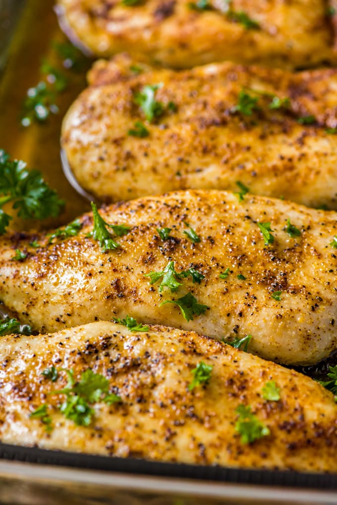 4 baked chicken breasts with seasoning and parsley in a clear baking dish