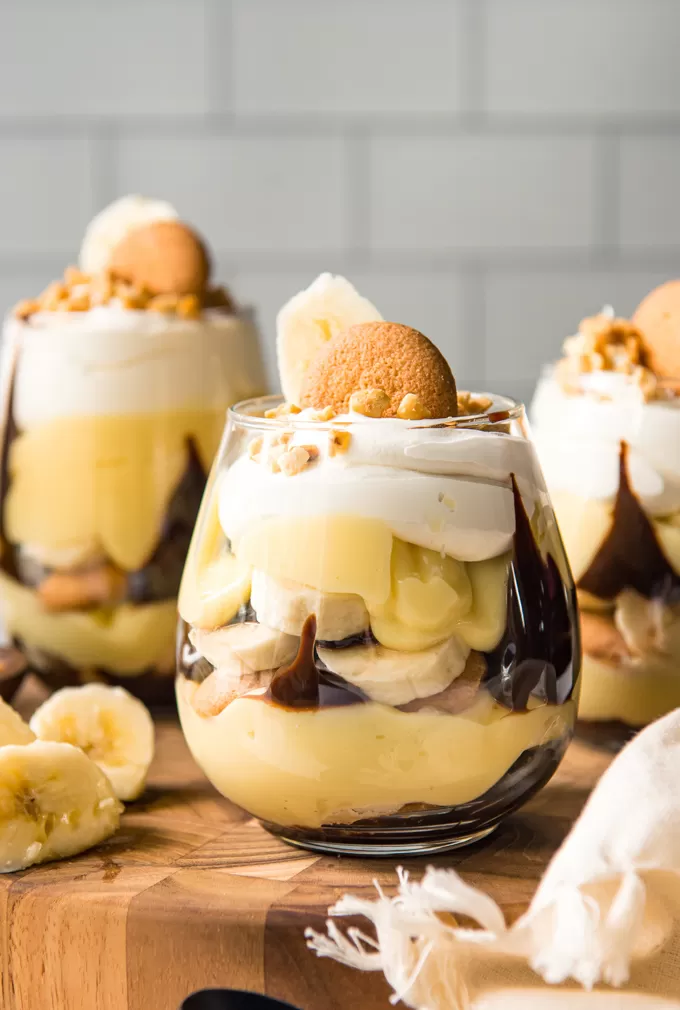Layered banana pudding cups with chocolate and peanuts in three separate glasses