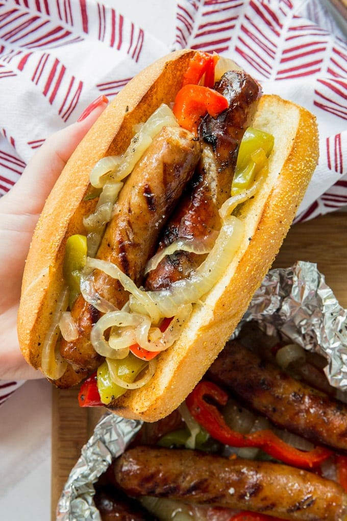 A hand holding a roll filled with grilled sausages, peppers and onions.