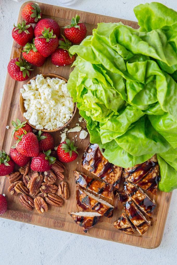 Lettuce leaves, strawberries, cheese and balsamic chicken spread on a cutting board - ingredients to make balsamic chicken lettuce wraps