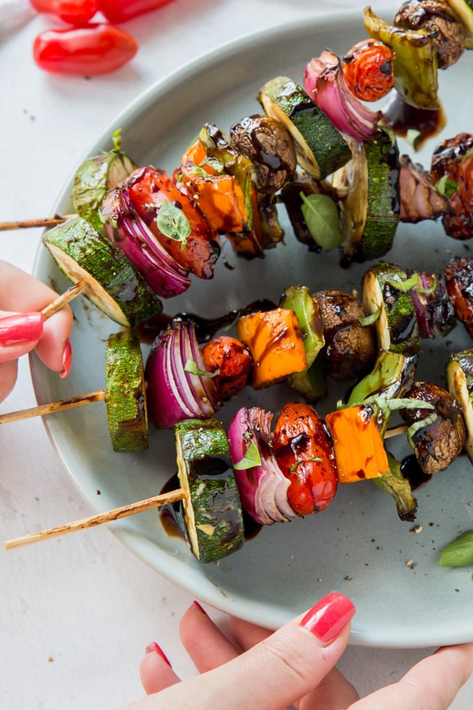 A hand reaching in to take a vegetable skewer