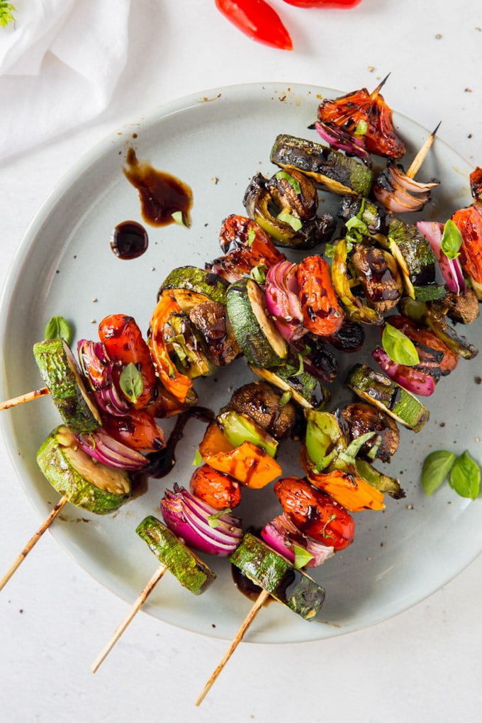 An overhead shot of grilled vegetables coated with a balsamic glaze and threaded on skewers.