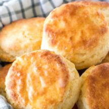 A bowl of flaky, buttery homemade biscuits with a tea towel to keep them warm.