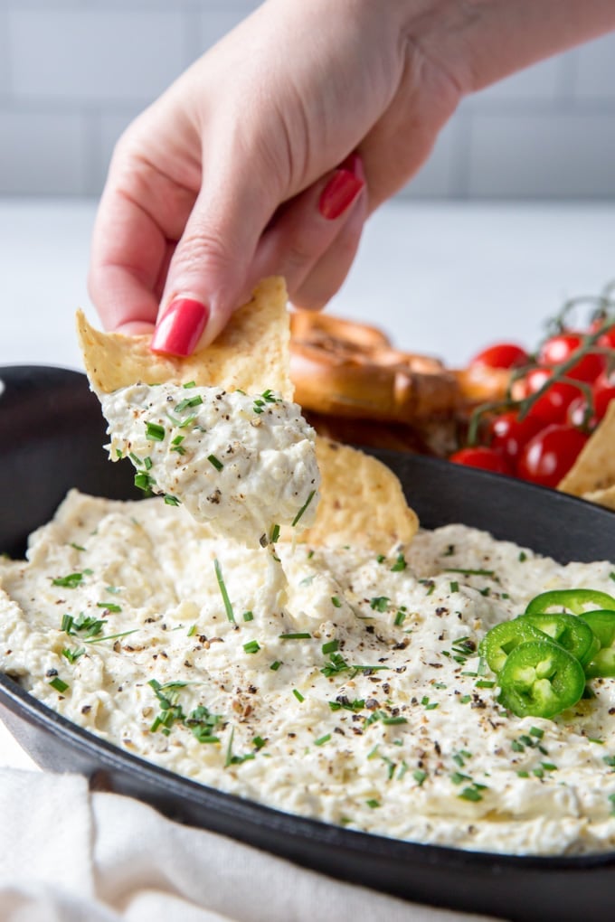 A hand dipping a tortilla chip into jalapeno artichoke dip