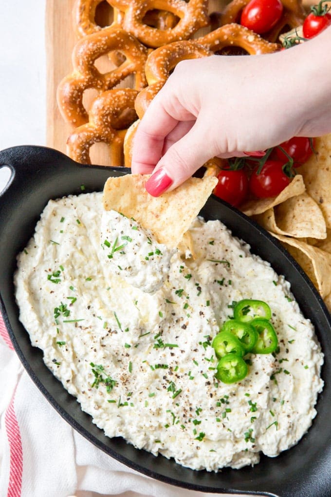 A hand reaching in and dipping a tortilla chip into a bowl of jalapeno artichoke dip