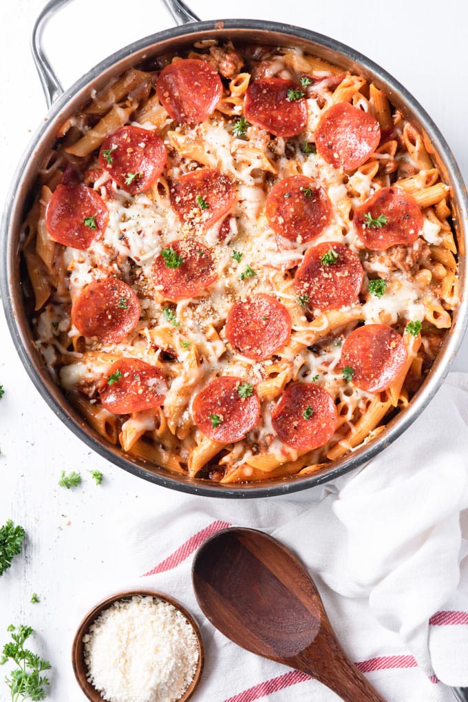 A pizza pasta casserole in a skillet on a white background, with Pasta and Pepperoni, a white napkin with red stripe