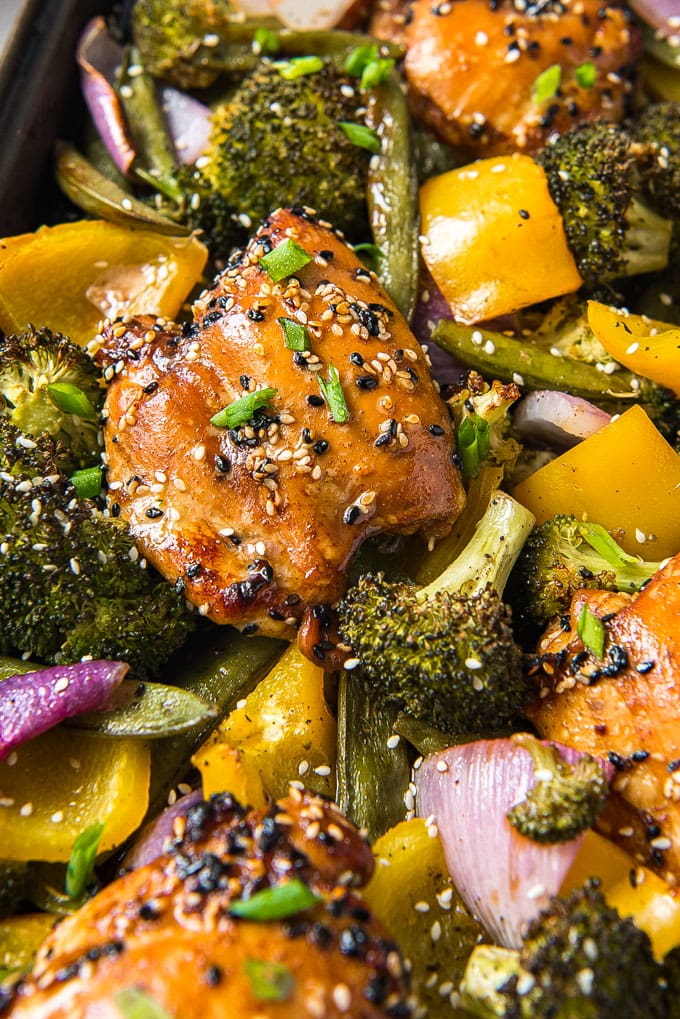 A close up of a chicken thigh with sesame chicken marinade and vegetables.