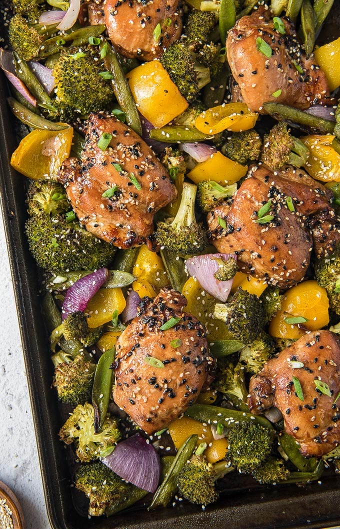 An overhead shot of sesame chicken and coloful vegetables on a sheet pan.