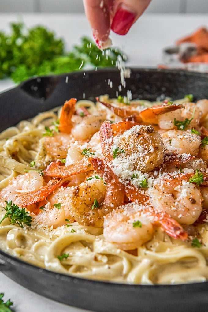 A hand sprinkling parmesan cheese over shrimp alfredo.