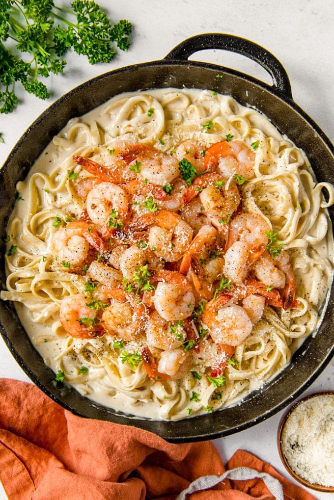 A large cast iron skillet full of fettuccine alfredo with shrimp.