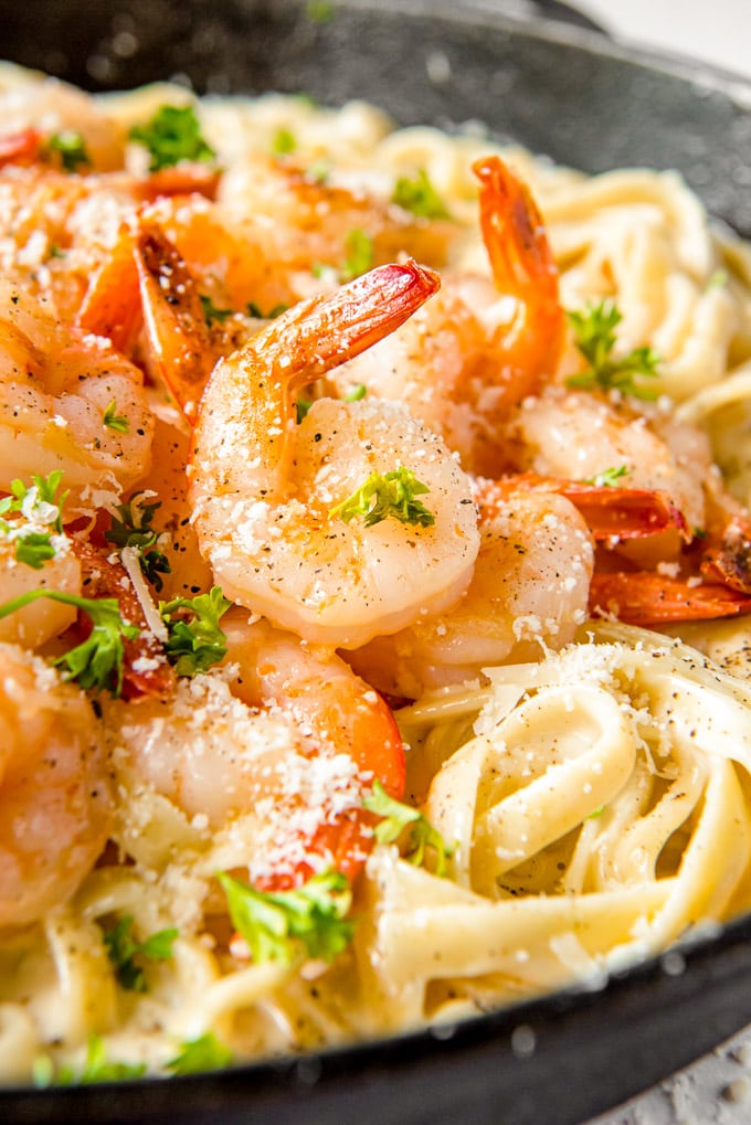 A close up of a shrimp sitting on top of a skillet of fettuccine alfredo.