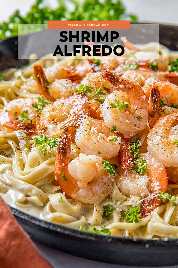 A skillet with fettuccine in alfredo sauce and topped with shrimp and parsley
