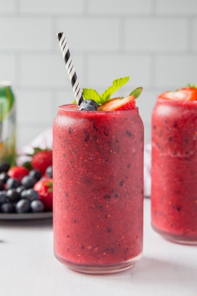 A close up image of a skinny berry smoothie in a glass with a can of diet 7up and fresh berries in the background.