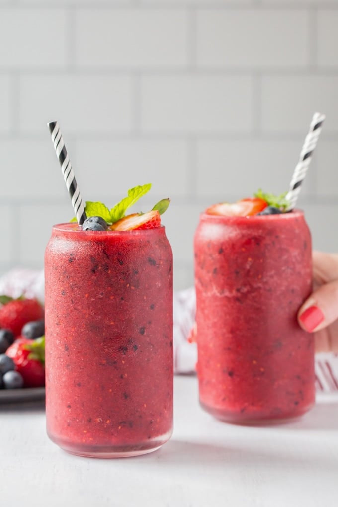 A hand reaches in to grab one of two glasses filled to the brim with a skinny berry smoothie mixture. 