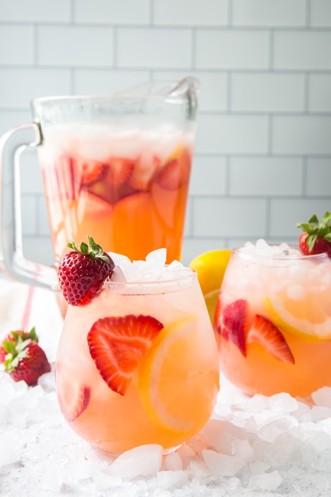 Strawberry Lemonade in two glasses and a pitcher surrounded by ice.