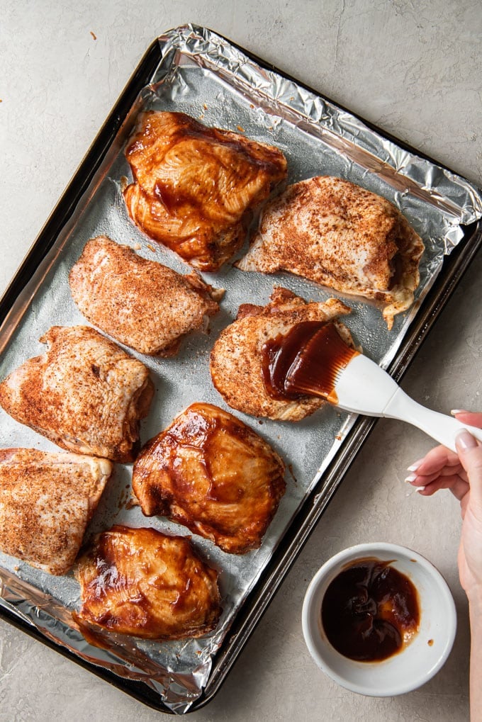 chicken thighs on a baking sheet as someone brushed one with barbecue sauce