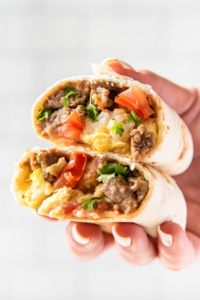 A hand holding two halves of a breakfast burrito together