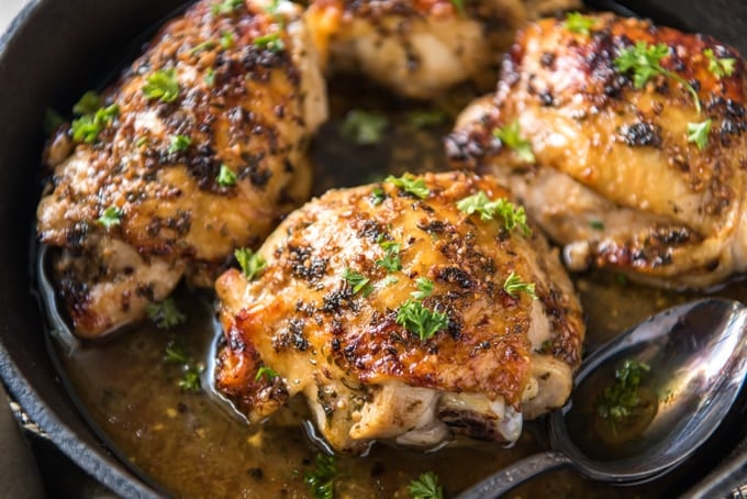 side view of roasted chicken thighs in black skillet, juices in pan, parsley garnish.