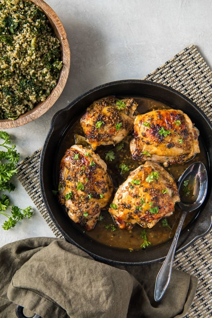 cast iron skillet, 4 roasted chicken thighs, silver spoon, bowl of quinoa