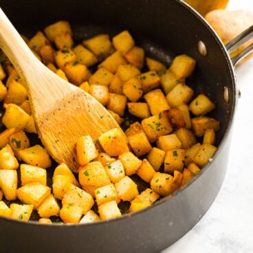 black saute pan with diced potatoes and parsley, wooden spoon.