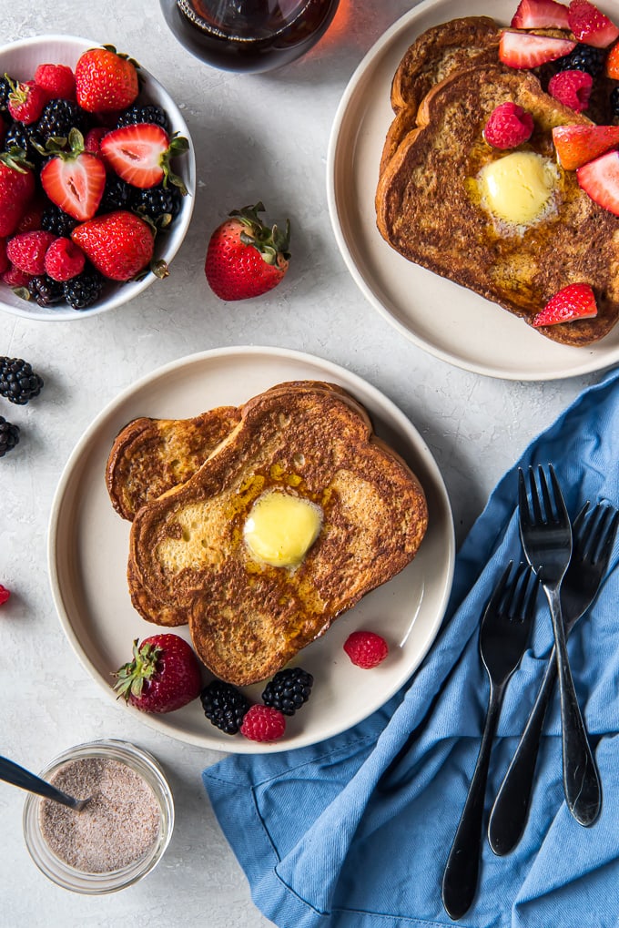 Two plates with french toast stacked with berries, a blue napkin and three forks.