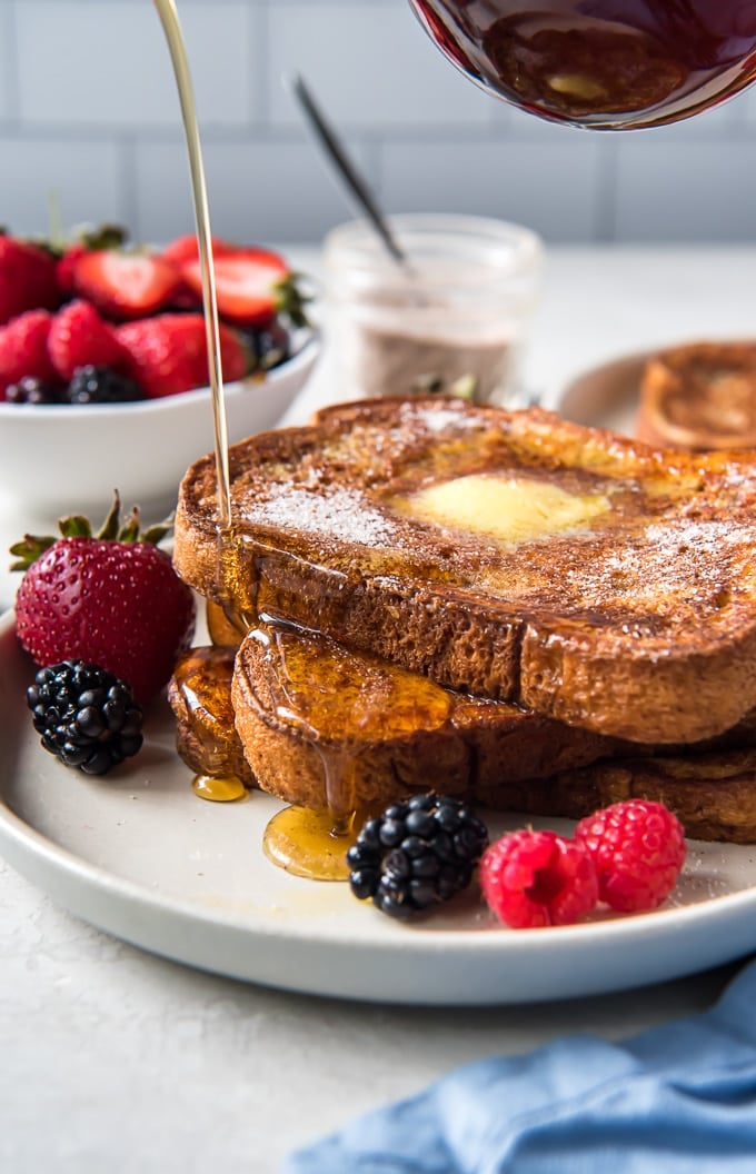 A side view of a stack of french toast with maple syrup being poured on top.