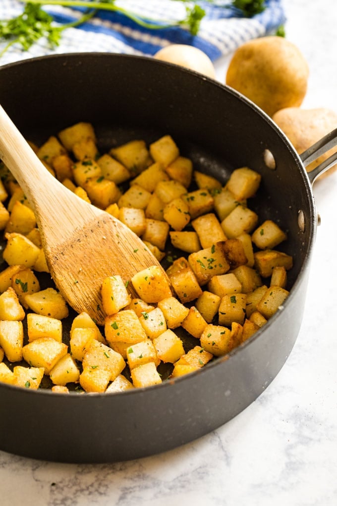 Skillet potatoes in a pan with a wooden spoon in it