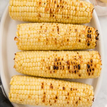 4 ears of grilled corn on the cob on a white plate. Image for social media.