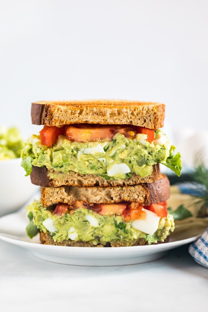 Two halves of an avocado egg salad sandwich stacked on top of each other revealing the center.