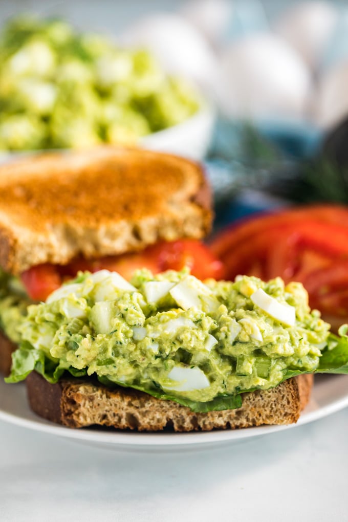 A half avocado egg salad sandwich with the top off revealing the egg salad.