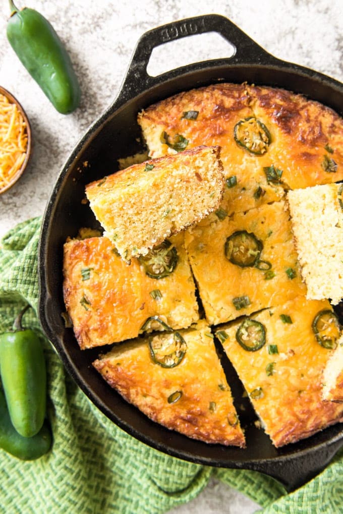 Cornbread with jalapenos in a skillet, sliced, with some pieces on their sides.