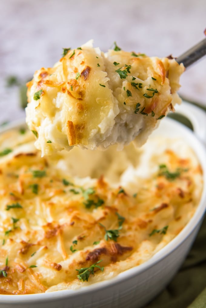 A large spoon scooping out a serving of cheesy mashed potatoes