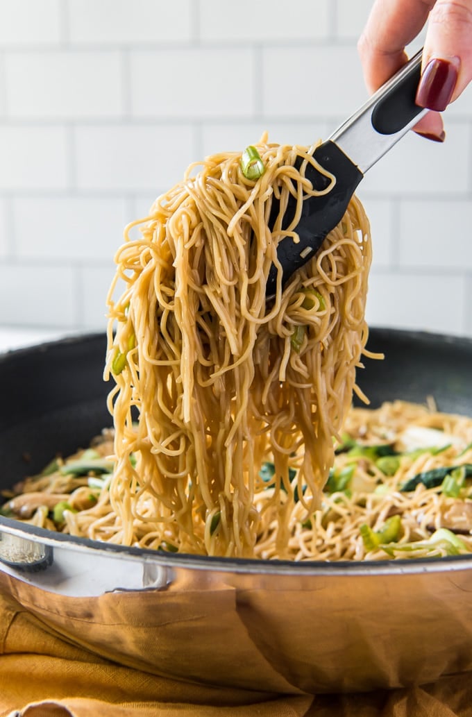 Chow mein noodles lifted out of the pan with tongs.