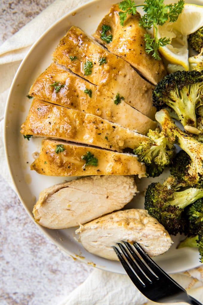 sliced mustard chicken breast, roasted broccoli on a white plate, fork. 